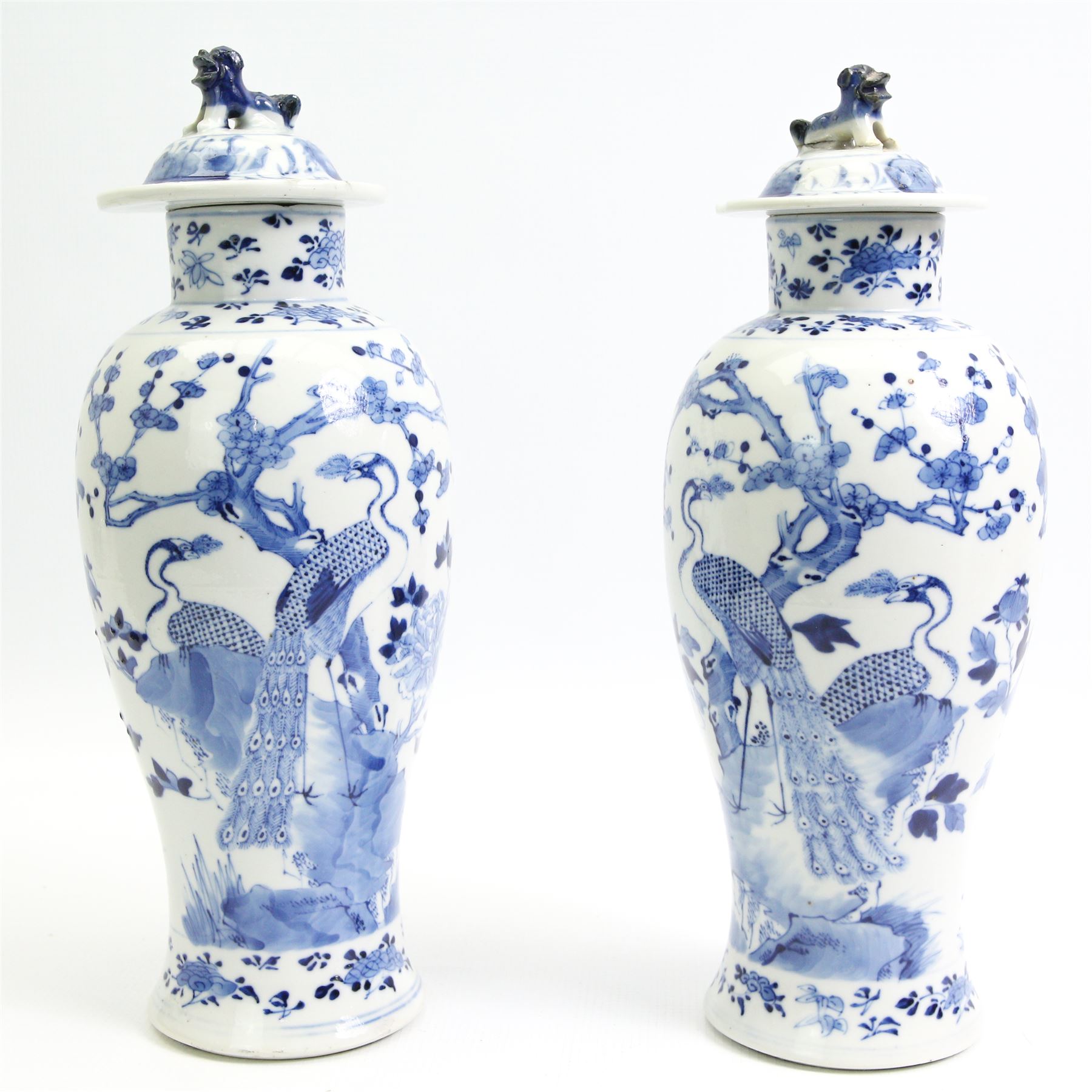 Pair of 19th/ early 20th century Chinese blue and white vases and covers, each of baluster form, painted in underglaze blue with peacocks stood on a rocky base amid blossoming peony and prunus flowers, the covers with dogs of fo finials, four character Kangxi marks beneath, H33cm 