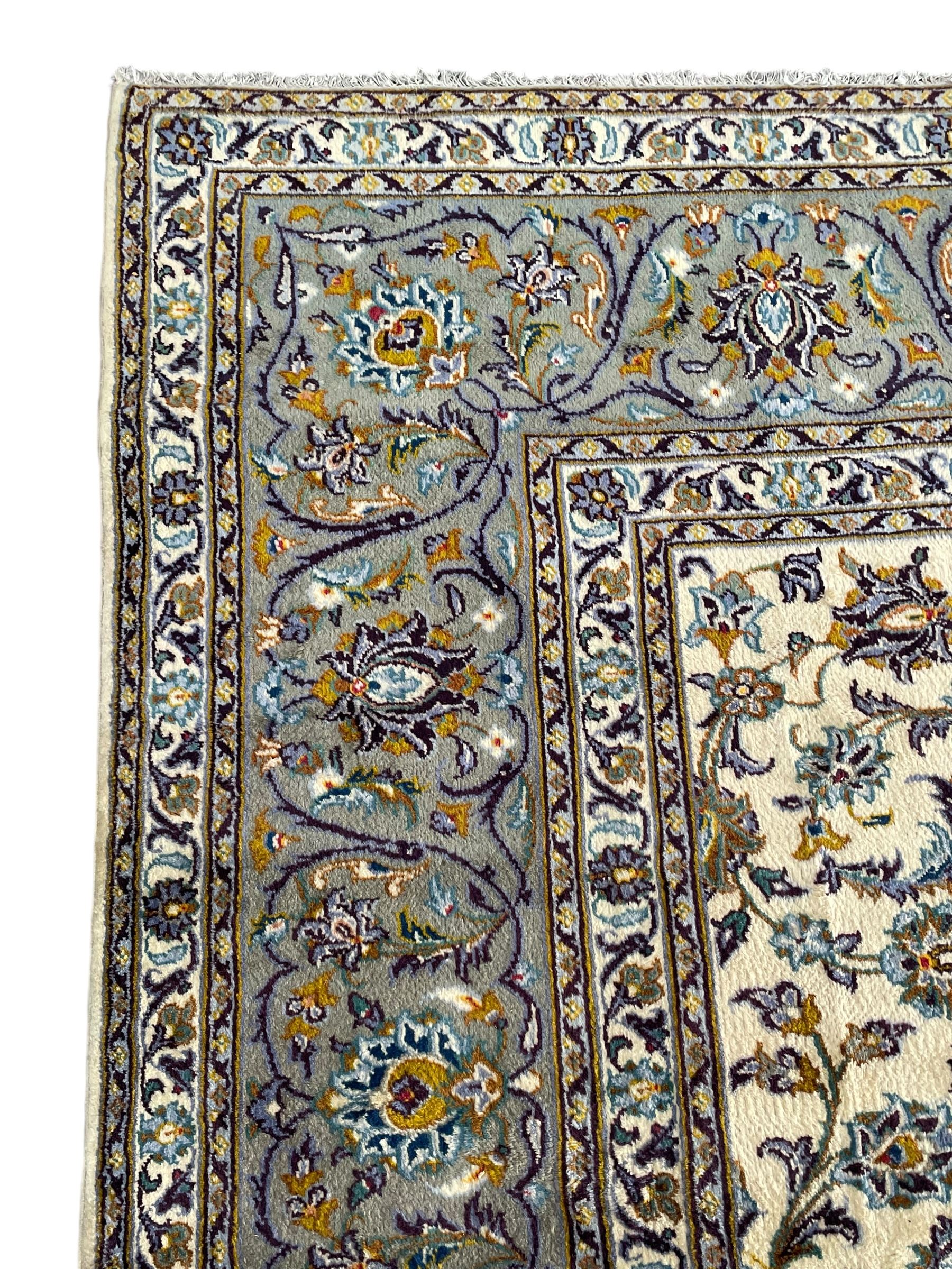 Persian Kashan ivory ground carpet, the busy field decorated with scrolling and interlaced leafy branches and palmettes, trailing branch border with repeating stylised plant motifs, within floral pattern guard stripes 