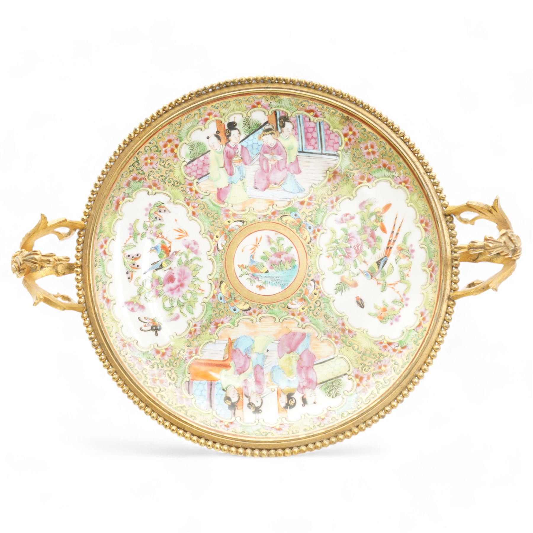 19th century Chinese Canton famille rose circular dish, painted with figures and exotic birds in shaped panels, against a floral and scroll ground, mounted in ormolu style gilt metal twin handled mount with beaded border and three scroll feet, W30cm x H14cm