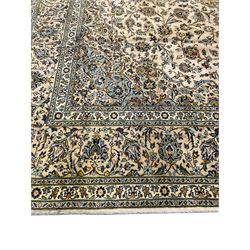 Central Persian Kashan pale khaki ground carpet, shaped central medallion enclosing small stylised motifs, the field decorated profusely with trailing foliate branches and plant motifs, guarded border with repeating floral design 