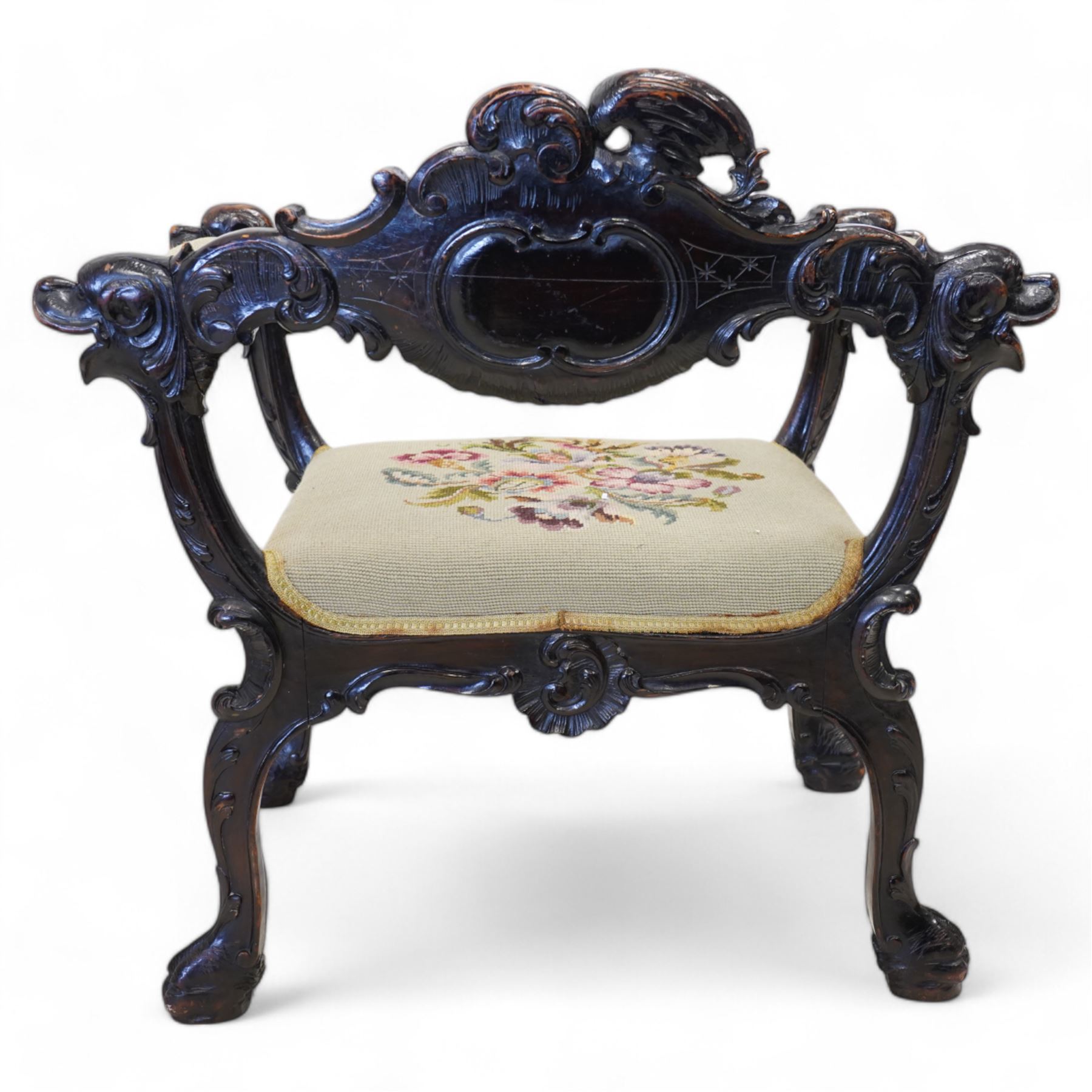 19th century Italian heavily carved stained walnut open armchair, the back rail carved with a large central cartouche decorated with extending acanthus and C-scroll motifs, the wing and arm terminals carved in the form of snarling dog masks, seat upholstered in floral needlework, shaped apron carved with cartouche and shell motifs, over out-splayed cabriole supports with acanthus moulding, terminating to paw feet