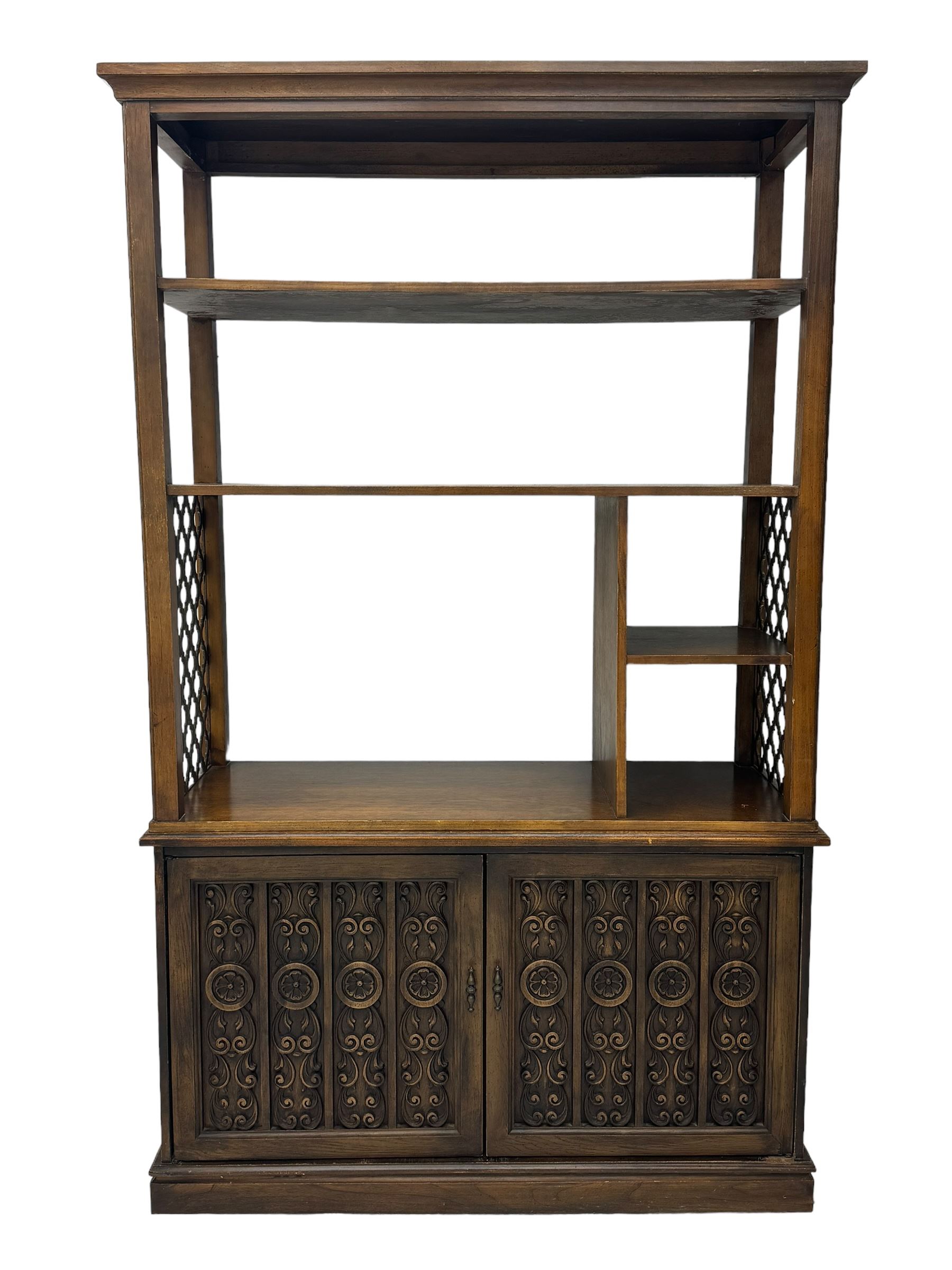 Mid 20th century oak bookcase cupboard, projecting cornice over three open shelves with subdivided sections and latticework uprights, two doors to the base with floral and scrollwork carvings and central brass handles, resting on a moulded plinth base