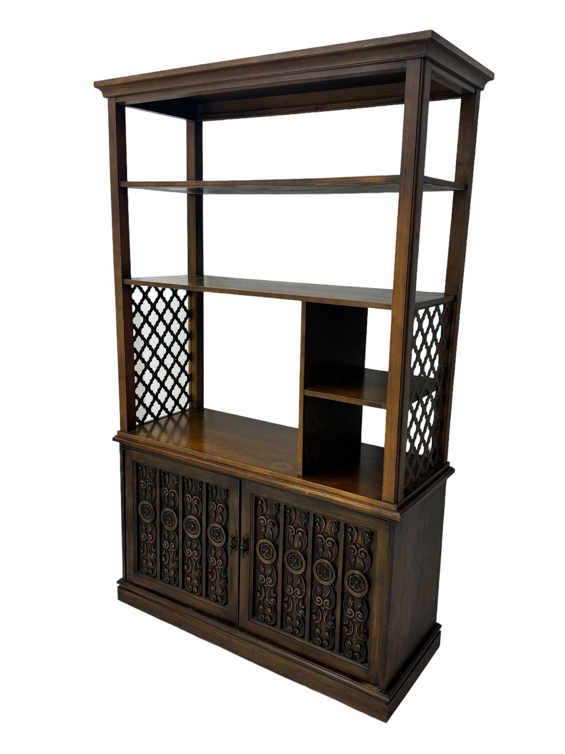 Mid 20th century oak bookcase cupboard, projecting cornice over three open shelves with subdivided sections and latticework uprights, two doors to the base with floral and scrollwork carvings and central brass handles, resting on a moulded plinth base