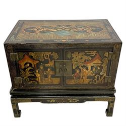 Pair of early 20th century Chinese ebonised and lacquered wood cabinets, the top decorated with dragons over lapping waves within a gilt patterned panel, the surrounding band decorated with Chinese symbols and flowerheads, enclosed by two doors each with village scenes with pagodas, figures and trees, the panelled sides decorated with a figure riding a dragon on stands with gilt decorated 