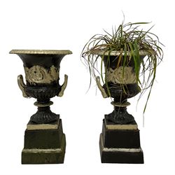 Pair of 20th century cast iron Campana-shaped urns on plinths, in ebonised and parcel-gilt painted finish