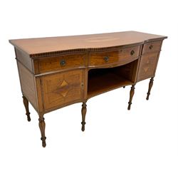 Waring & Gillow - Edwardian Sheraton Revival satinwood sideboard, shaped and stepped break bow-front, the top with central oval book-matched veneered panel and rosewood banding, the front and return edges inlaid with a single row of repeating circles, three frieze drawers each inlaid with rosewood band and ebony stringing, two cupboards flanking open centre, the doors inlaid with lozenges and satinwood cross bandings, on faceted octagonal supports with foliate carved collars, terminating to turned feet, the central drawer with 'Warings' metal plaque and stamped 'Gillows'