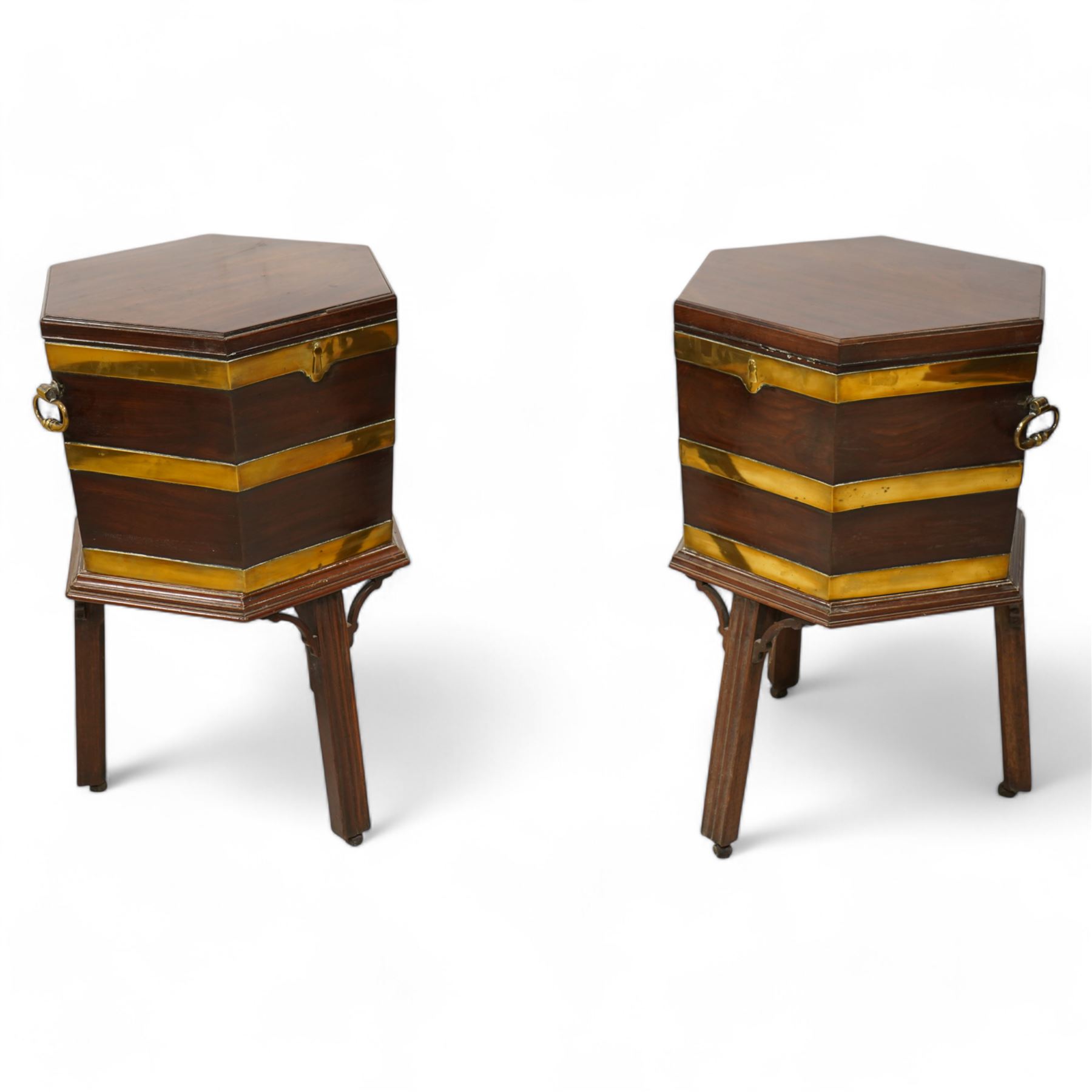 Pair of George III mahogany and brass bound cellarettes or wine coolers on stands, hexagonal form, moulded hinged lid enclosing metal lining, the body strapped in brass bands and fitted with carrying handles, the stand with moulded upper rails on splayed and moulded square supports with castors, with arched corner brackets 