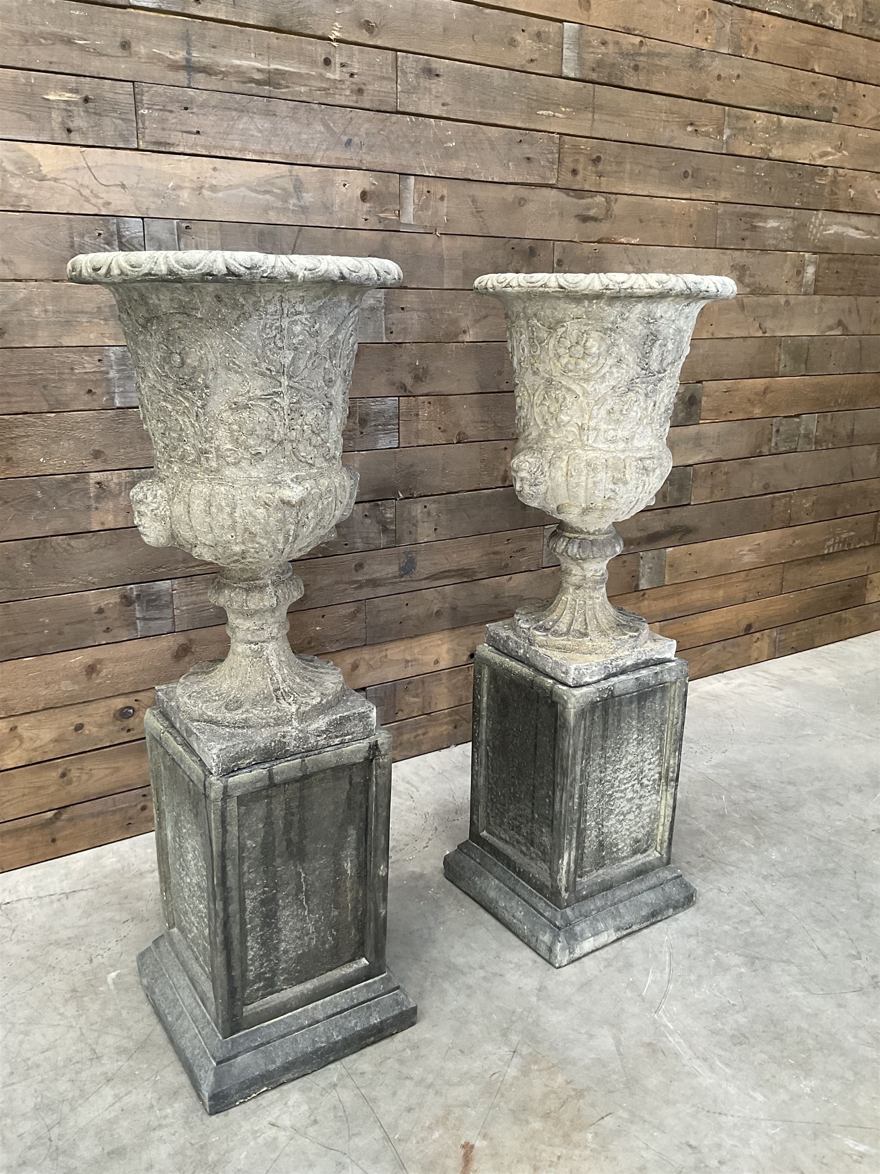 Pair of Georgian design cast stone garden urns, egg and dart rim with raised floral motifs, pedestal base terminating on square plinth, raised on square block plinth