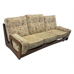 Mid-20th century three-seat sofa with floral patterned upholstery, supported by a sculpted teakwood frame with curved cutout detailing, loose cushioned back and seat, on tubular metal feet