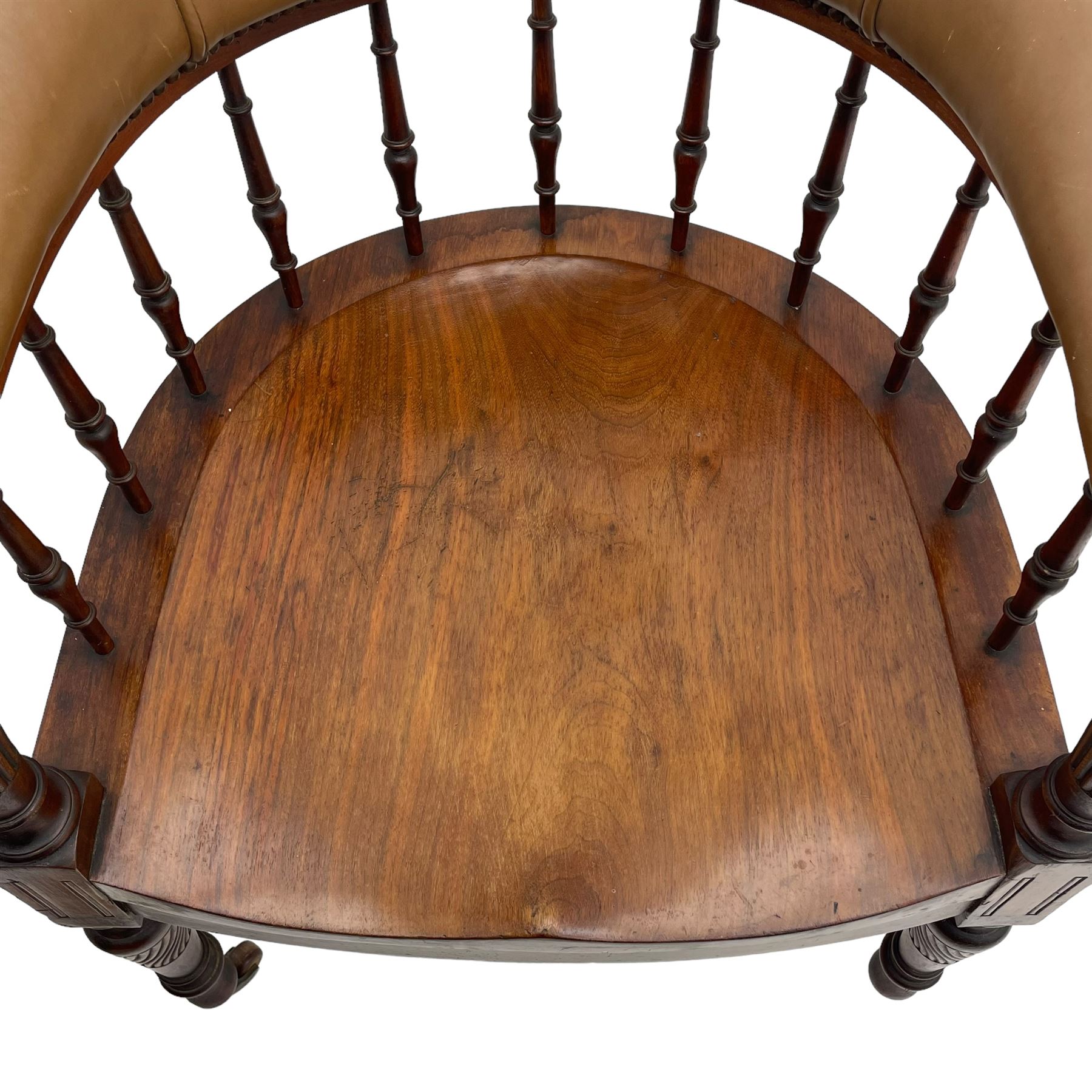 Pair of late Victorian walnut tub-shaped elbow chairs, the cushioned cresting rail upholstered in leather on spindle turned supports, dished saddle seat on turned supports