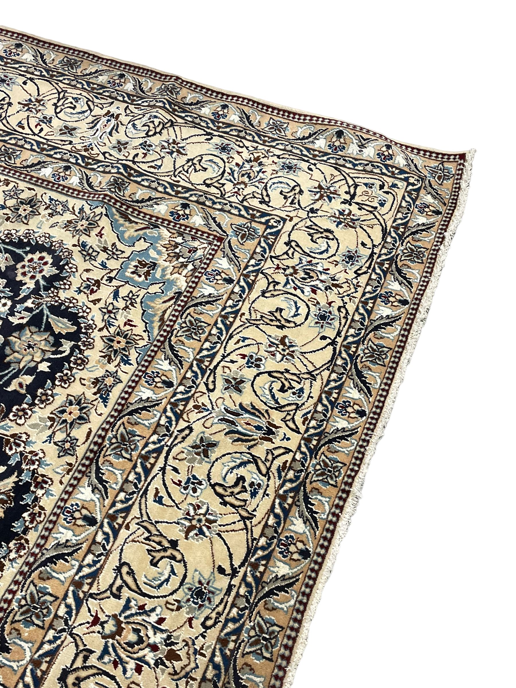 Persian Kashan indigo ground carpet, the central ivory rosette medallion surrounded by trailing and interlaced flower heads and branches, matching spandrels with floral design, the border with scrolling pattern decorated with stylised plant motifs within guards