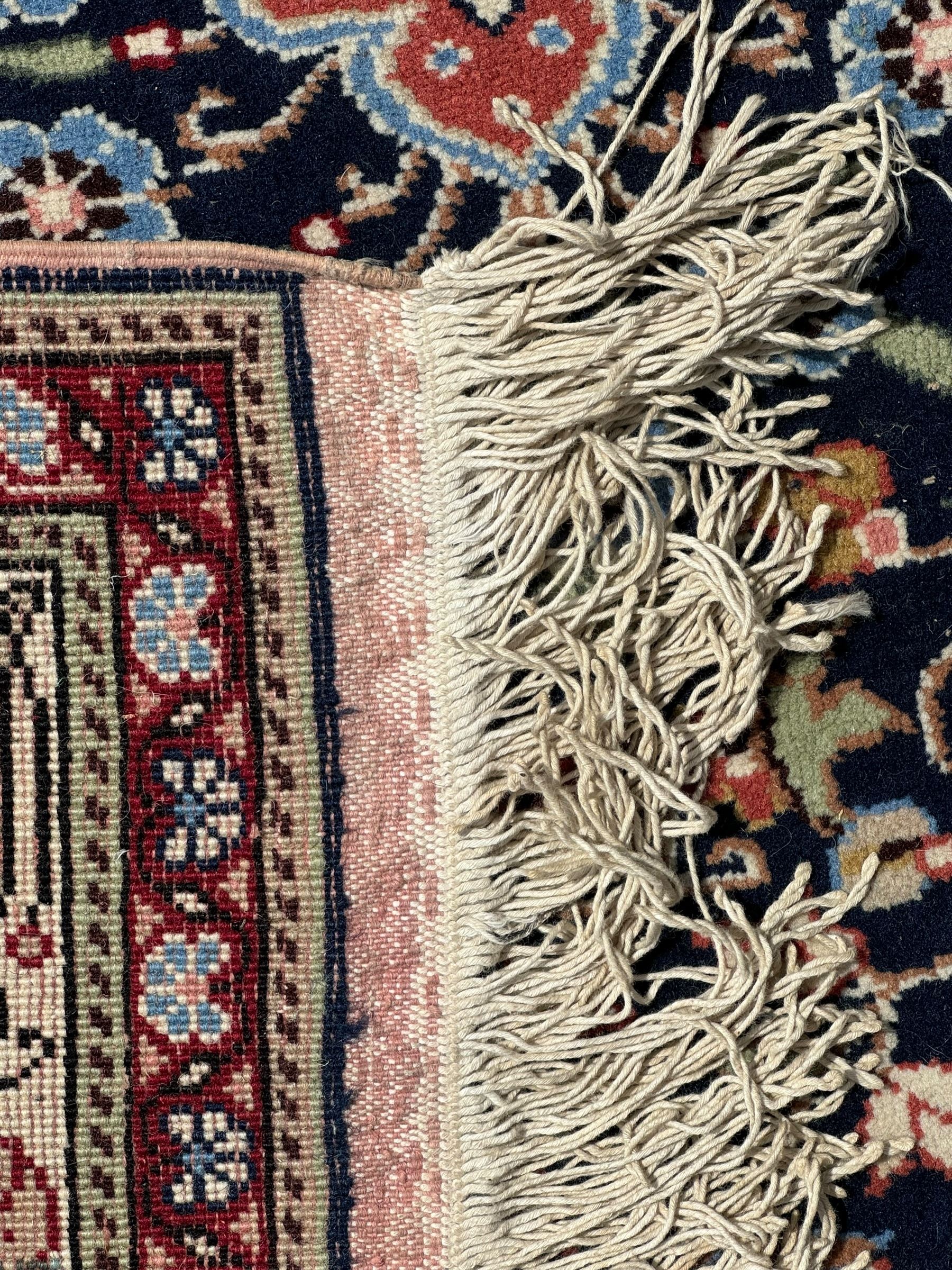 Indo-Persian indigo ground rug, the floral design peach medallion surrounded by trailing and interlaced branches and flower heads, the main border decorated with repeating stylised plant motifs within floral guard stripes 