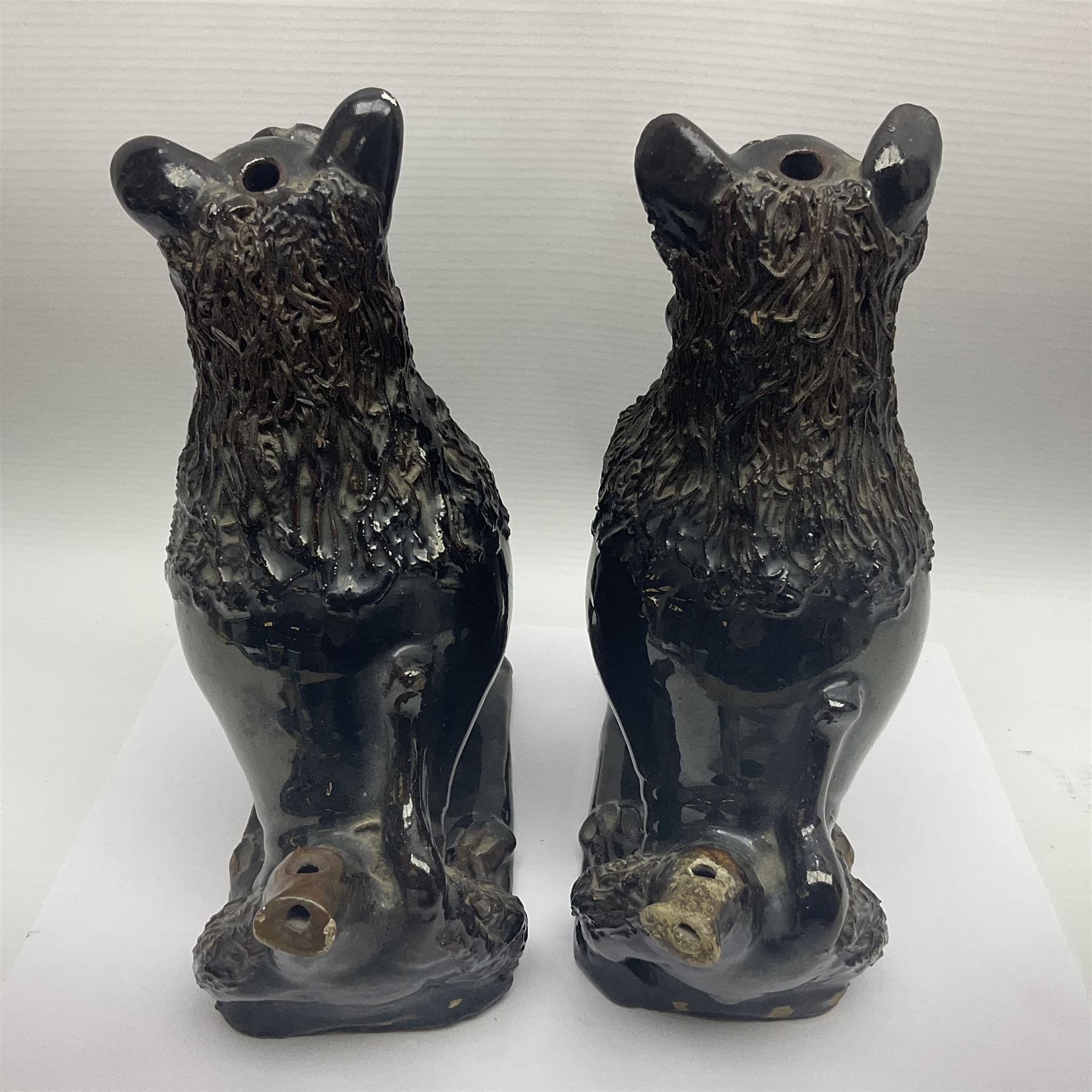 Pair of unusual early English pottery figures, modelled in the form of seated dogs with baskets between their jaws, the tails forming whistles, each upon rectangular base, overall H22cm