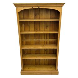 Pine open bookcase, projecting moulded cornice over arched frieze, fitted with four adjustable shelves, on plinth base