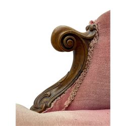 Victorian walnut framed tete-a-tete loveseat, scrolled arm terminals with moulded foliate decoration, buttoned backs and sprung seat upholstered in pale pink velvet, raised on cabriole supports with applied flower heads and scroll feet terminating to ceramic castors