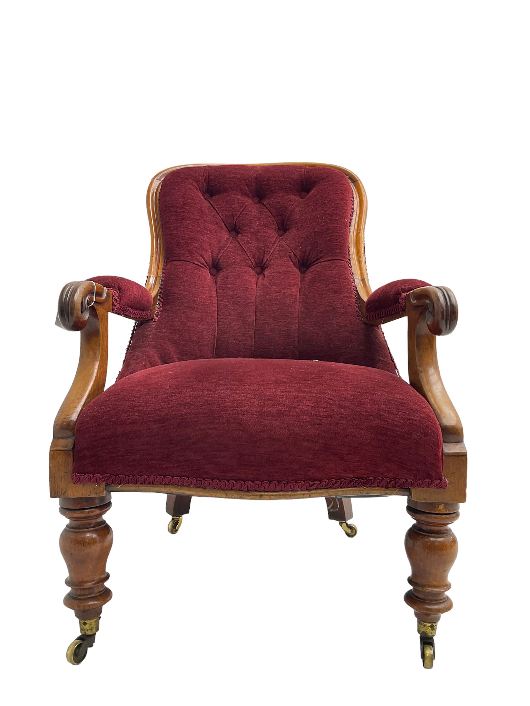 Victorian mahogany framed open armchair, upholstered in buttoned red fabric, the arm terminals carved with scrolls, on turned front supports with brass cups and castors