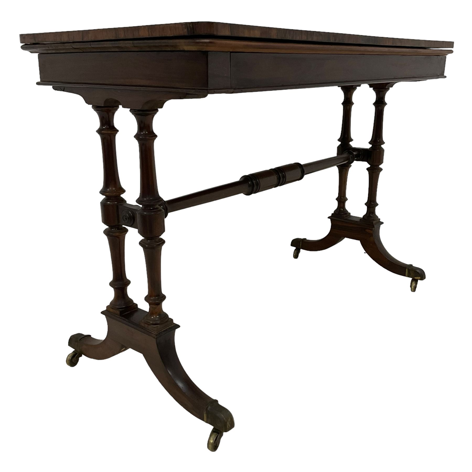 Regency rosewood card table, fold-over swivel action rectangular top with crossbanding, single frieze drawer, raised on turned end supports terminating in splayed feet with castors, joined by ring turned stretcher