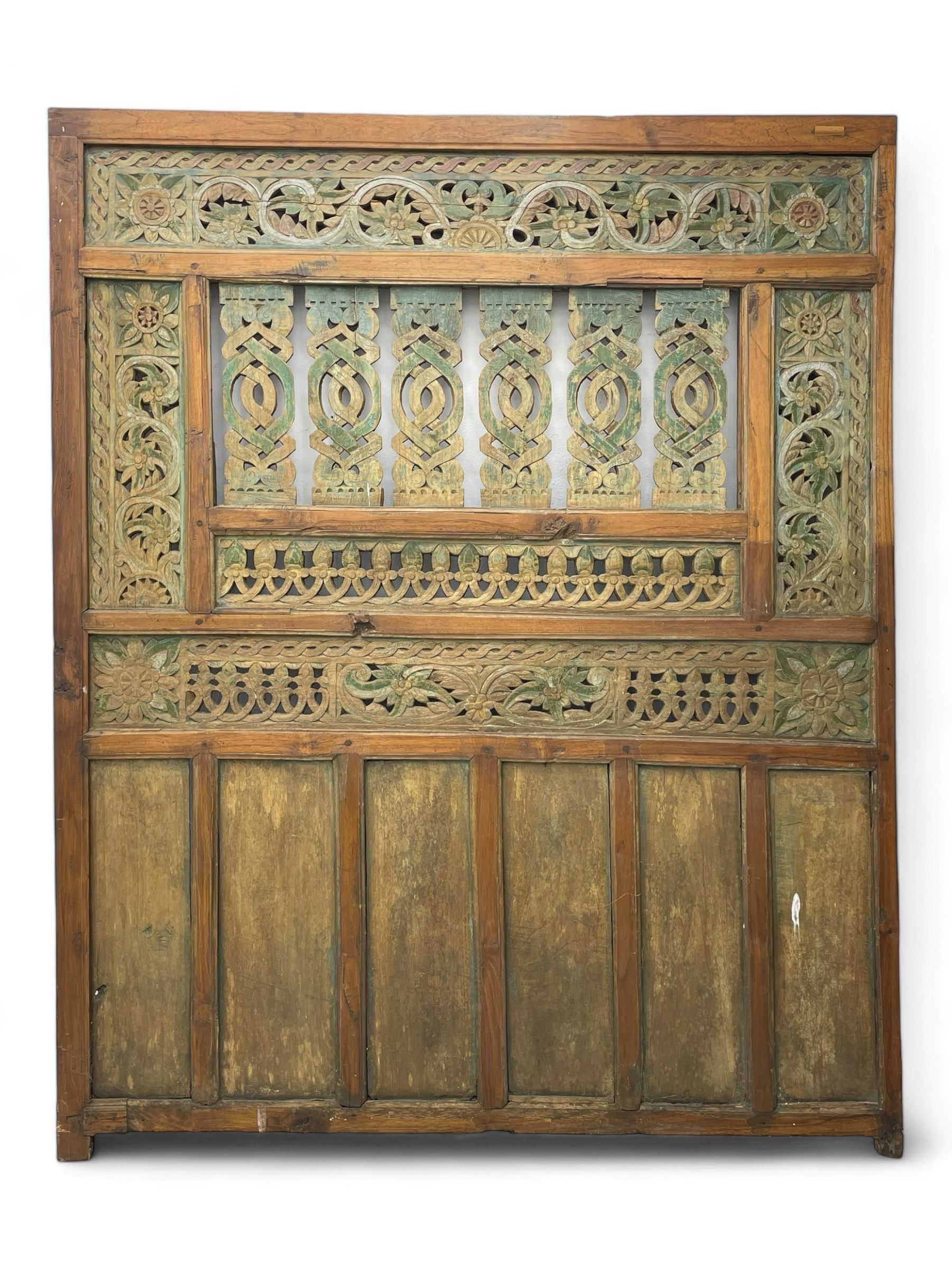 Early 20th century Javanese teak and hardwood door panel or room divider, rectangular panelled form with moulded frame and pegged construction, carved and pierced with scrolling decoration and flower head motifs, shaped and pierced splats with interlocking pattern