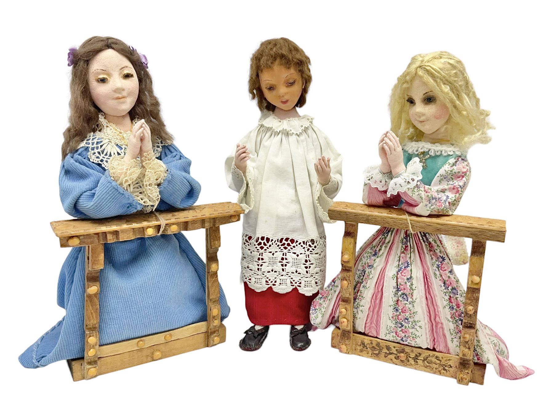 Anna Meszaros Hungary - two hand made needlework figurines, each of a young girl kneeling by an alter rail praying H28cm; together with another similar of a chorister H29cm (3)  Auctioneer's Note: Anna Meszaros came to England from her native Hungary in 1959 to marry an English businessman she met while demonstrating her art at the 1958 Brussels Exhibition. Shortly before she left for England she was awarded the title of Folk Artist Master by the Hungarian Government. Anna was a gifted painter of mainly portraits and sculptress before starting to make her figurines which are completely hand made and unique, each with a character and expression of its own. The hands, feet and face are sculptured by layering the material and pulling the features into place with needle and thread. She died in Hull in 1998.