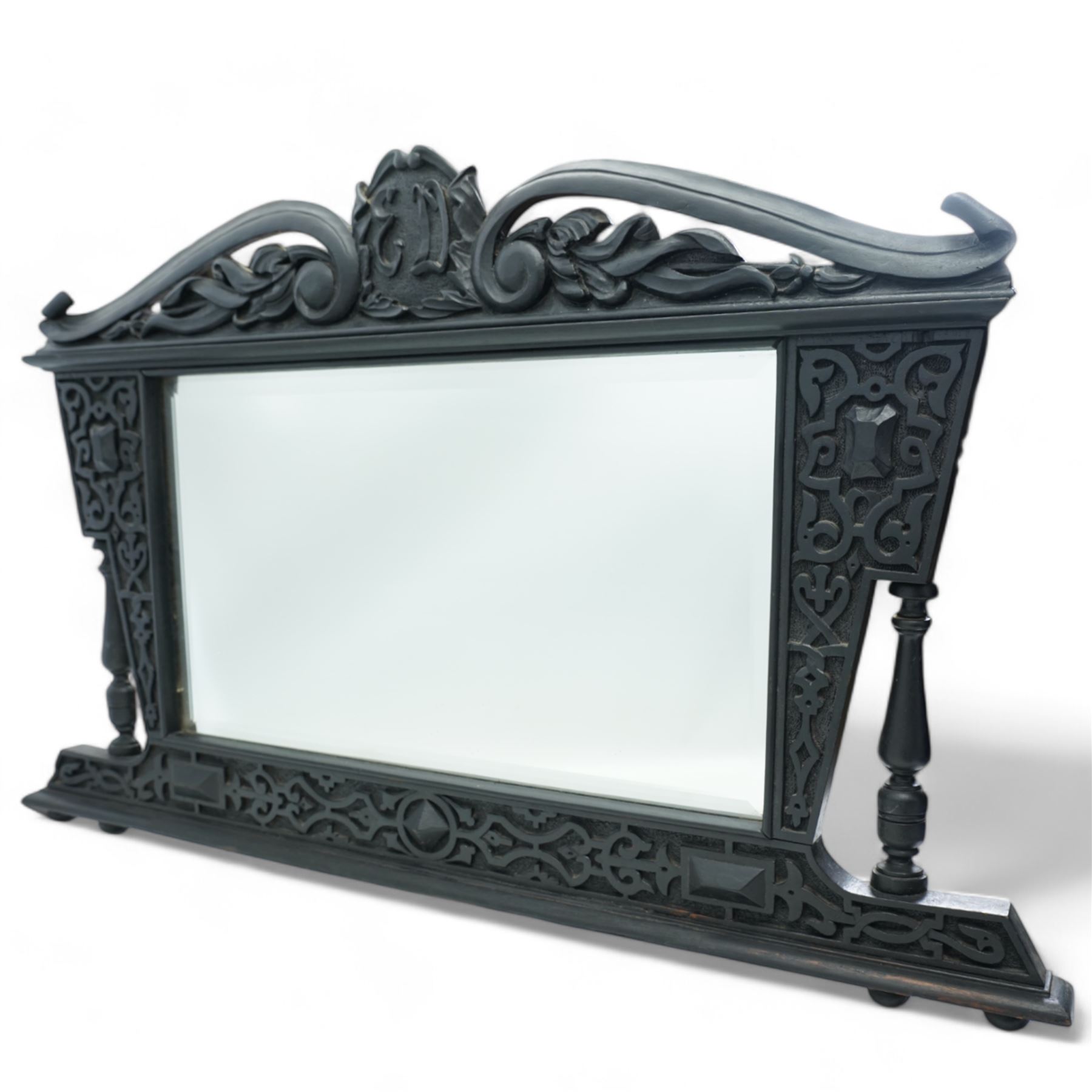 Late Victorian black painted mahogany wall mirror, scrolled pediment with central cartouche inscribed 'E.D', carved strapwork brackets and lower rail with turned supports, bevelled mirror plate 