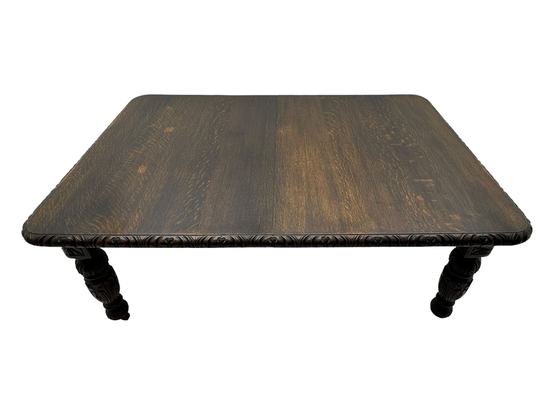 19th century heavily carved oak extending dining table, rectangular top with rounded corners and carved gadrooned edge, extending via winding mechanism with two additional leaves, raised on acanthus leaf-carved baluster supports terminating in ceramic castors