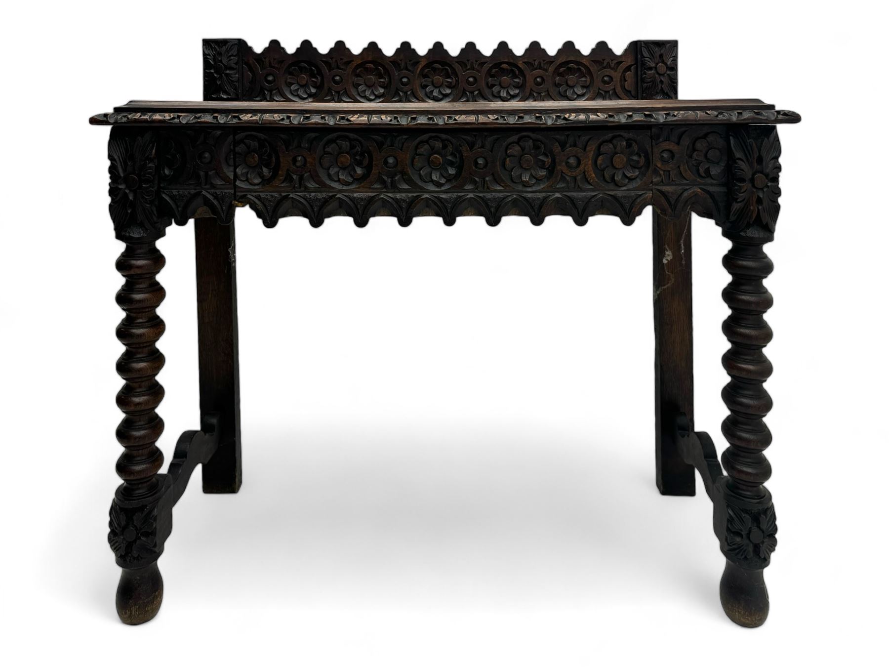 Victorian Gothic revival style carved oak console table, rectangular top with carved edge and raised back gallery, over deeply carved apron with floral and foliate motifs and central drawer, barley twist front supports and plain rear supports united by shaped stretchers, on front bun feet