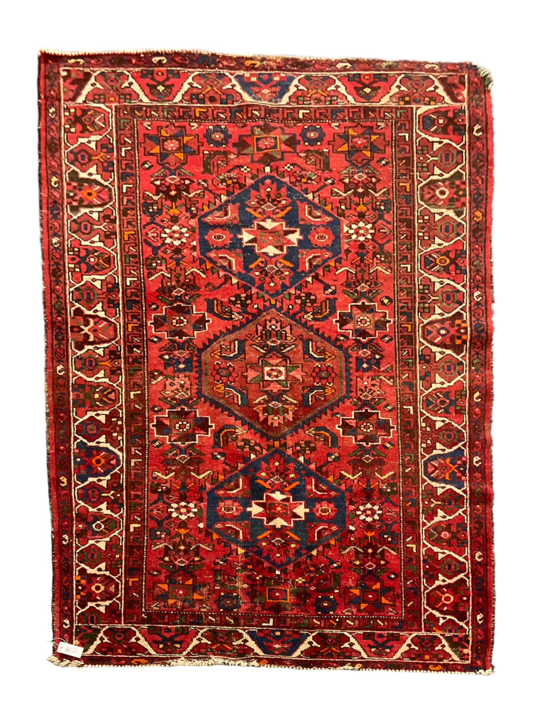 Persian Hamadan rug, red ground with overall geometric design, the field with three extended lozenges, decorated with geometric and stylised flower head motifs, the border and guards decorated with repeating geometric motifs