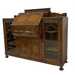 Early 20th century heavily carved oak bookcase bureau, raised back with grape-vine carved frieze, over fall-front enclosing fitted interior, above two short drawers and curved frieze drawer, flanked by astragal glazed and panelled cupboards, on turned feet