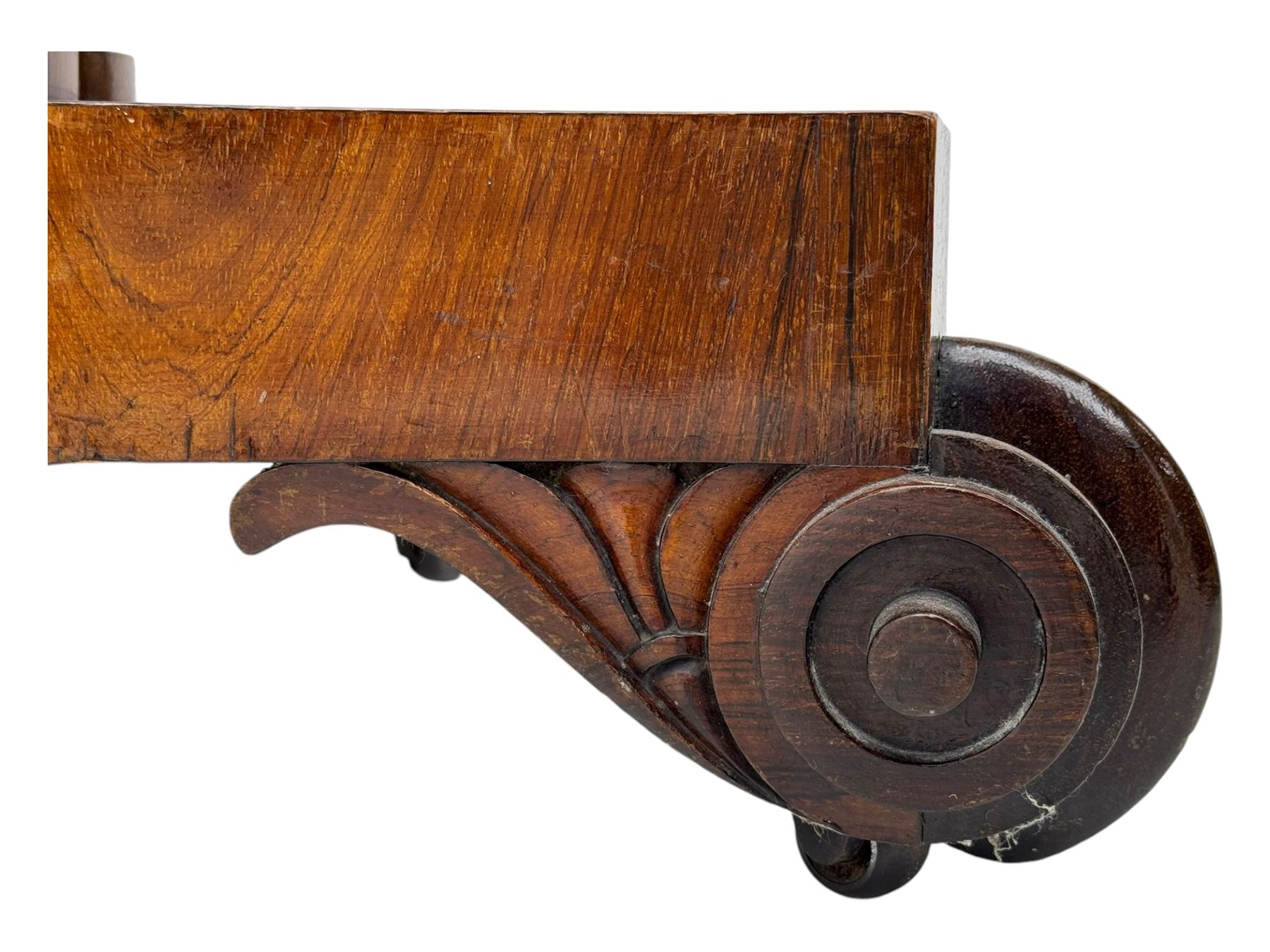 Early Victorian rosewood card table, rectangular foldover swivel top with rounded corners, red baize-lined surface, frieze adorned with carved foliate motifs, supported by a central octagonal waisted column on shaped quatrefoil base, terminating in scrolled feet with concealed metal castors