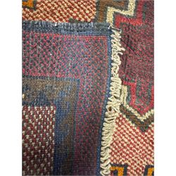 Baluchi crimson ground rug, the central field decorated with two stacked geometric lozenge medallions, surrounded by stepped multicoloured motifs, the wide border with alternating angular motifs in deep red, within a narrow brown guard stripe