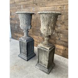 Pair of Georgian design cast stone garden urns, egg and dart rim with raised floral motifs, pedestal base terminating on square plinth, raised on square block plinth