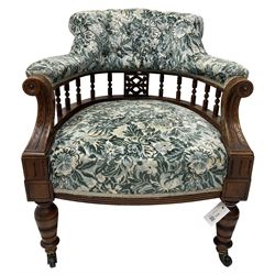 Victorian walnut framed tub-shaped armchair, the shaped rolled back supported by a spindle turned balustrade, upholstered in buttoned floral fabric, scrolled arms supports carved with acanthus leaves and flower heads, on collar turned feet with brass and ceramic castors