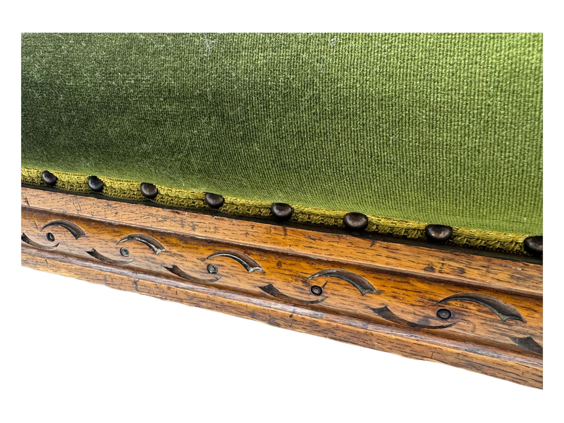 Late Victorian walnut framed sofa, rectangular backrest with carved detailing and central motif, upholstered in olive green fabric with brass studded trim and patterned front rail, scrolled fluted arms supported by turned uprights terminating in bun feet