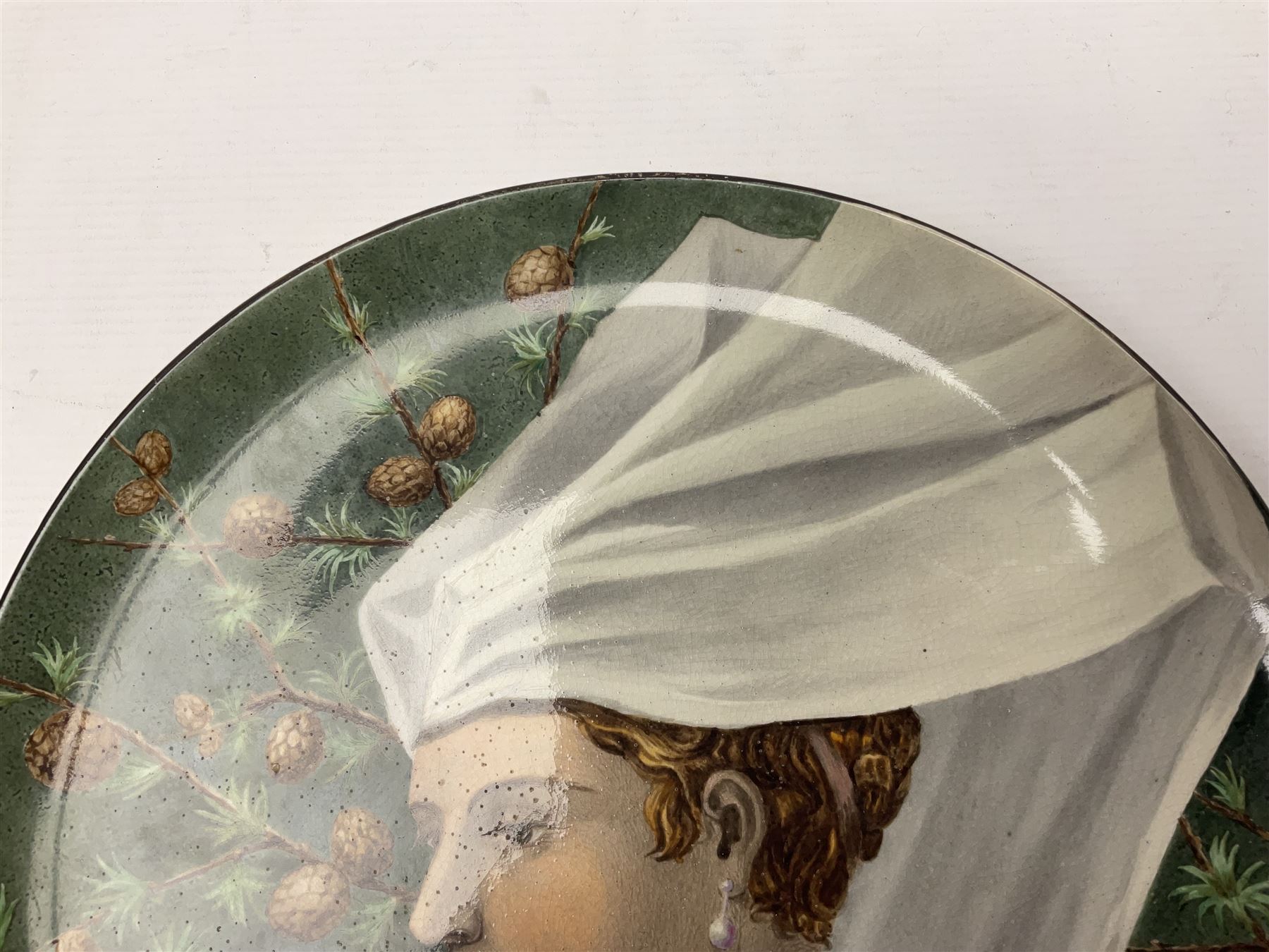 19th century continental pottery charger, depicting a woman in a white veil with pinecones on a green ground, with indistinct signature to the back, D31cm