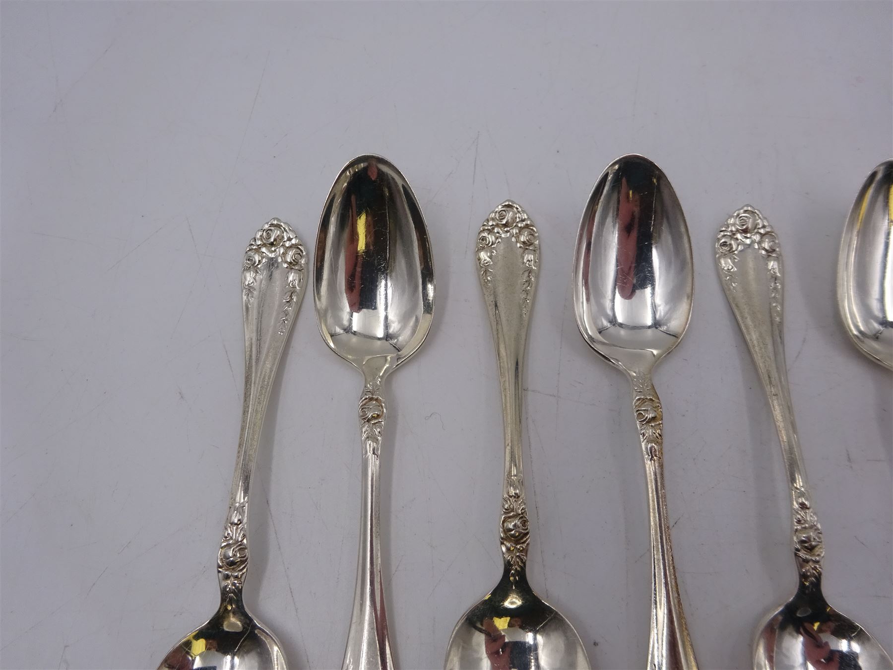 Two sets of twelve late 19th/ early 20th century American silver coffee spoons, the first set with engraved initial to terminal within scrolling border and engraved date verso, the second set with embossed floral decoration to handles, all stamped Sterling 