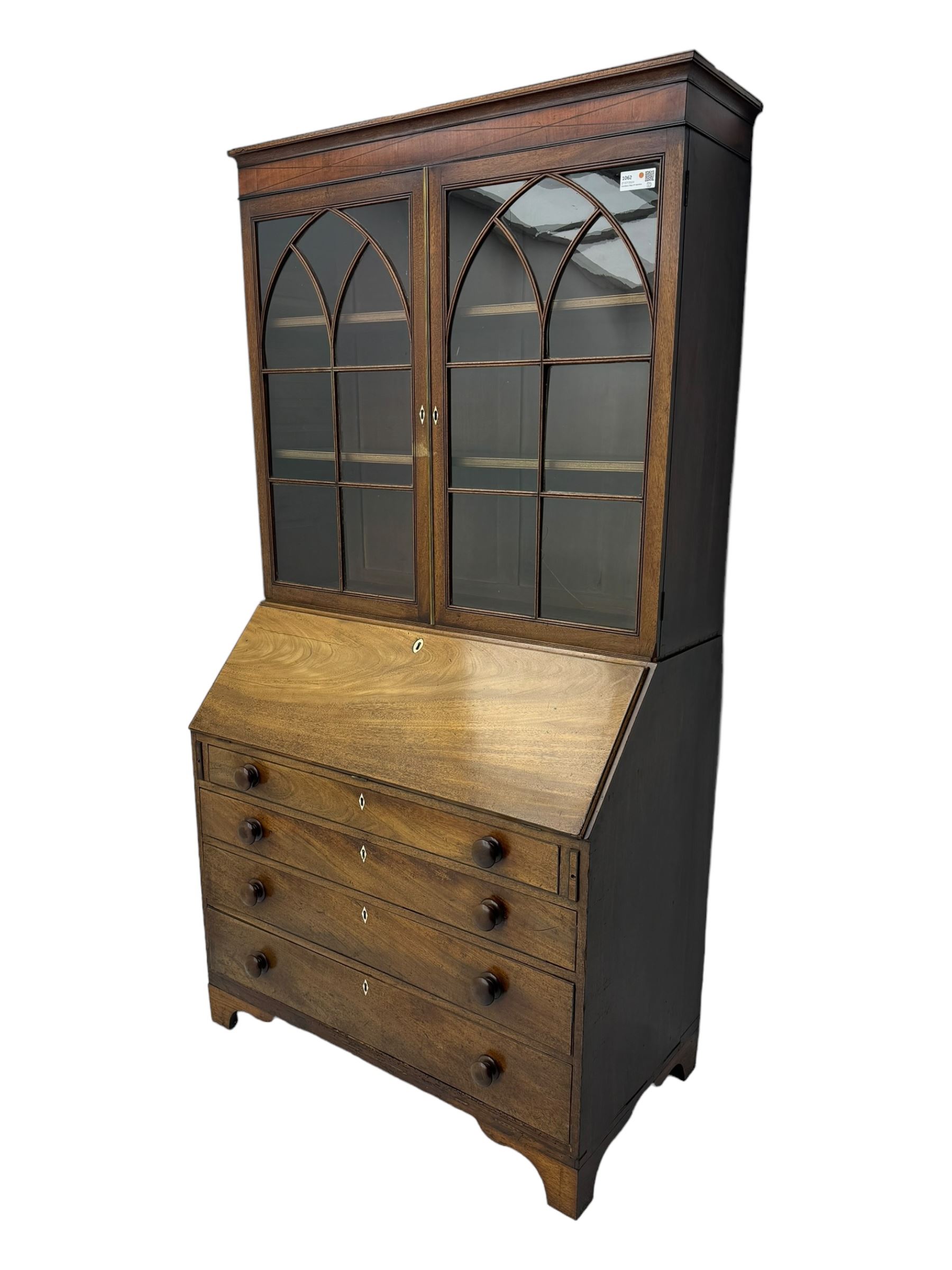 Early 19th century mahogany bureau bookcase, the projecting cornice over two Gothic-style astragal glazed doors enclosing two adjustable shelves, sloped hinged lid enclosing fitted interior and felt inset, four graduating drawers, on bracket feet