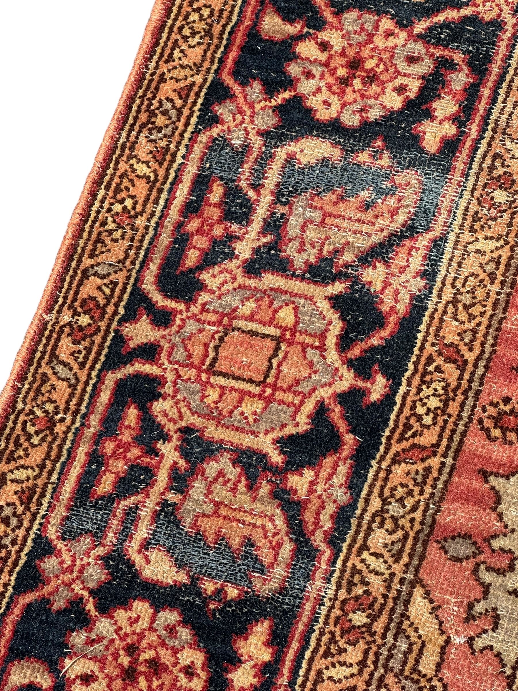 Persian Heriz design rug with red ground, the field featuring a central medallion with floral and geometric motifs, surrounded by ivory spandrels, the main border showcasing a series of floral patterns on a dark blue ground