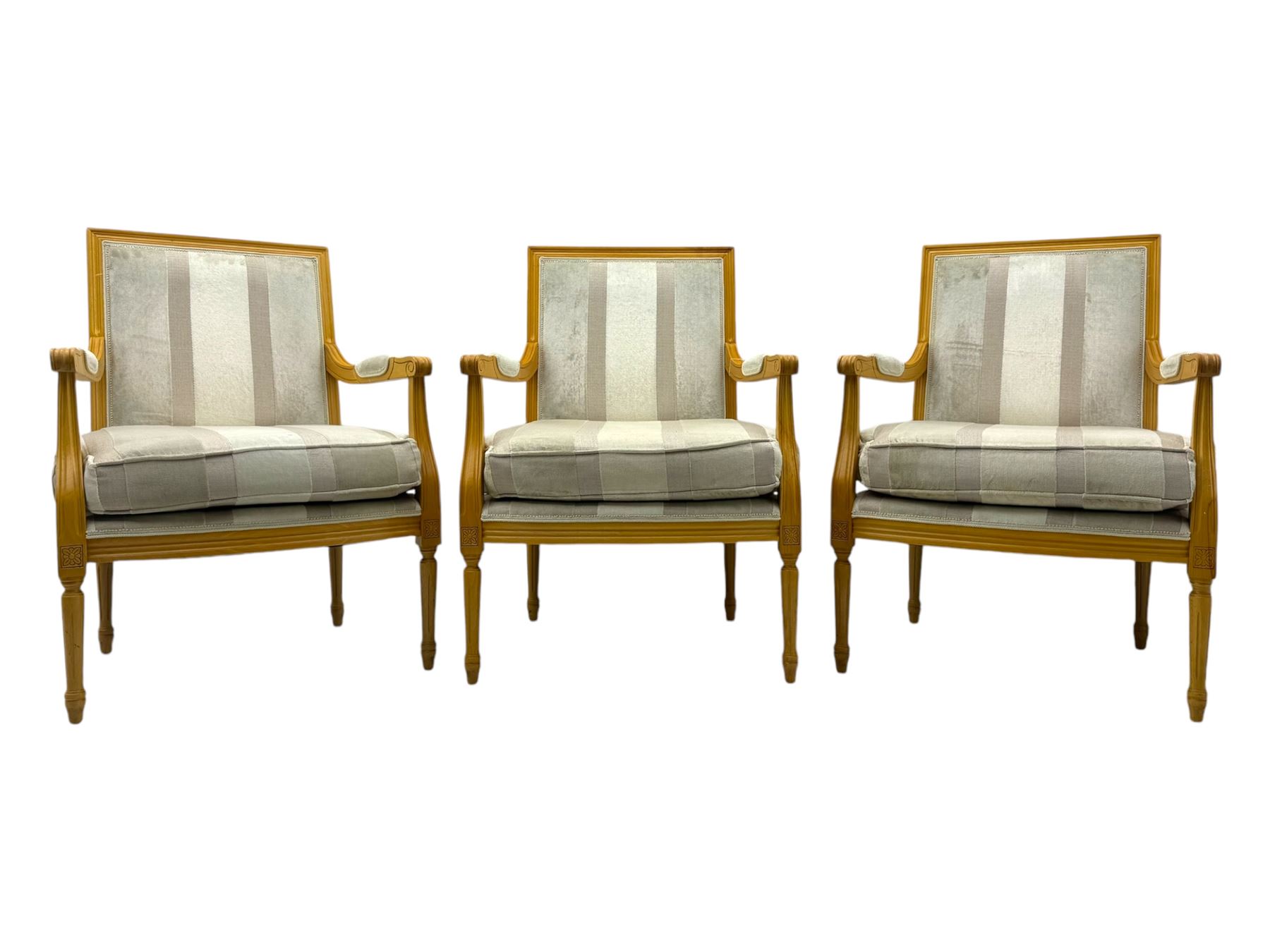 Three mid-20th century beechwood fauteuil armchairs, upholstered backrest and seat in cream stripe fabric, padded armrests with scroll detail, on tapered fluted supports with carved floral rosette blocks