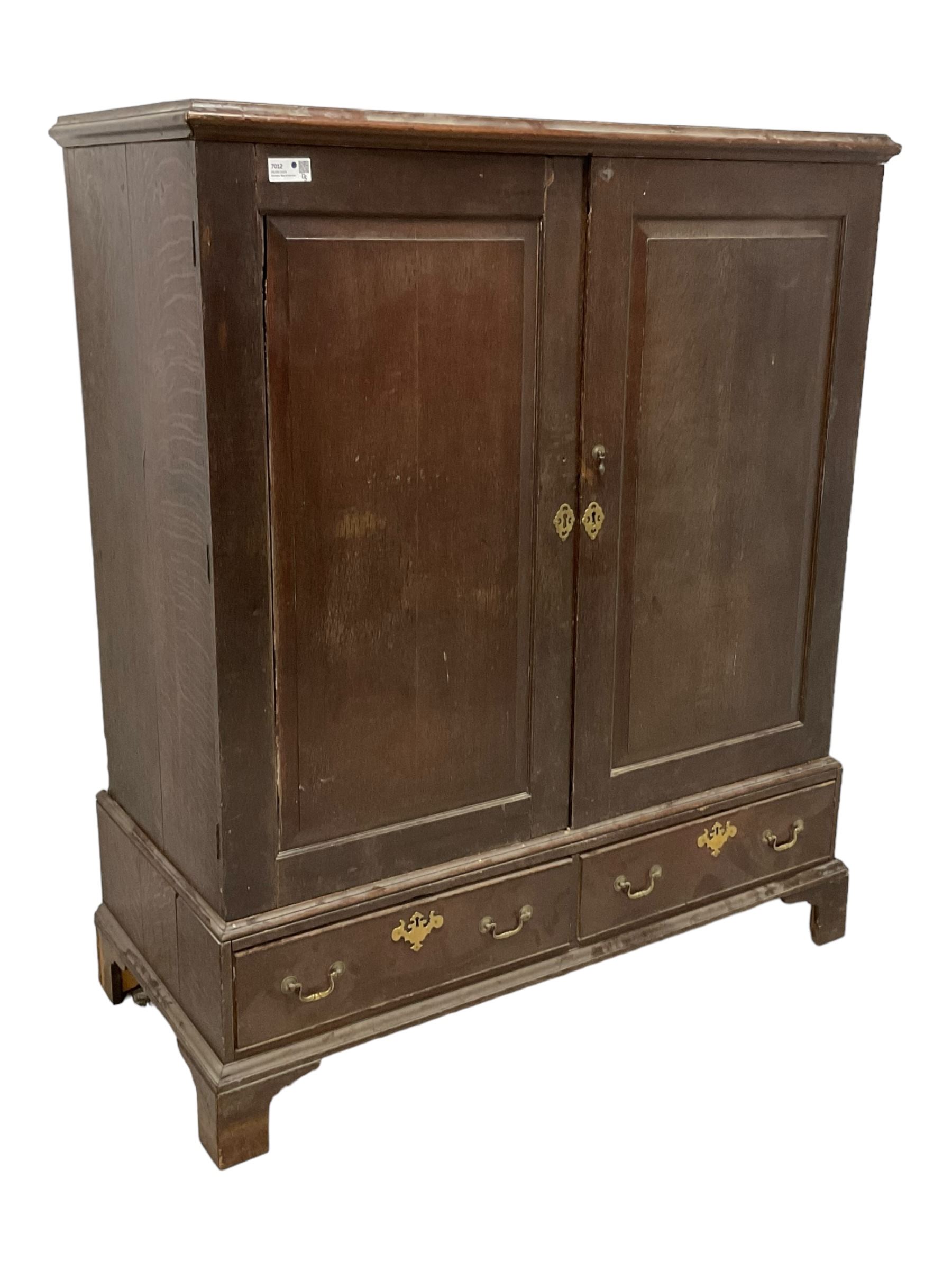 18th century oak linen press, moulded cornice over two panelled cupboard doors, the base fitted with two cock-beaded drawers with pieced brass escutcheons and handles, lower moulded edge on bracket feet