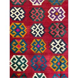 Southwest Persian Qashqai Kilim red ground rug, the central field adorned with rows of multicolored hexagonal medallions with geometric patterns, the border featuring alternating black and white stepped diamonds, narrow band to one end decorated with multicoloured geometric figures