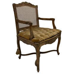 Late 19th century French carved beech open elbow chair, shaped cresting rail carved with central shell and curl leafage, cane work seat and back with buttoned loose seat cushion, the open arms carved with scrolled terminals and acanthus leaves, on cabriole supports with carved decorated united by shaped and moulded x-framed stretchers 