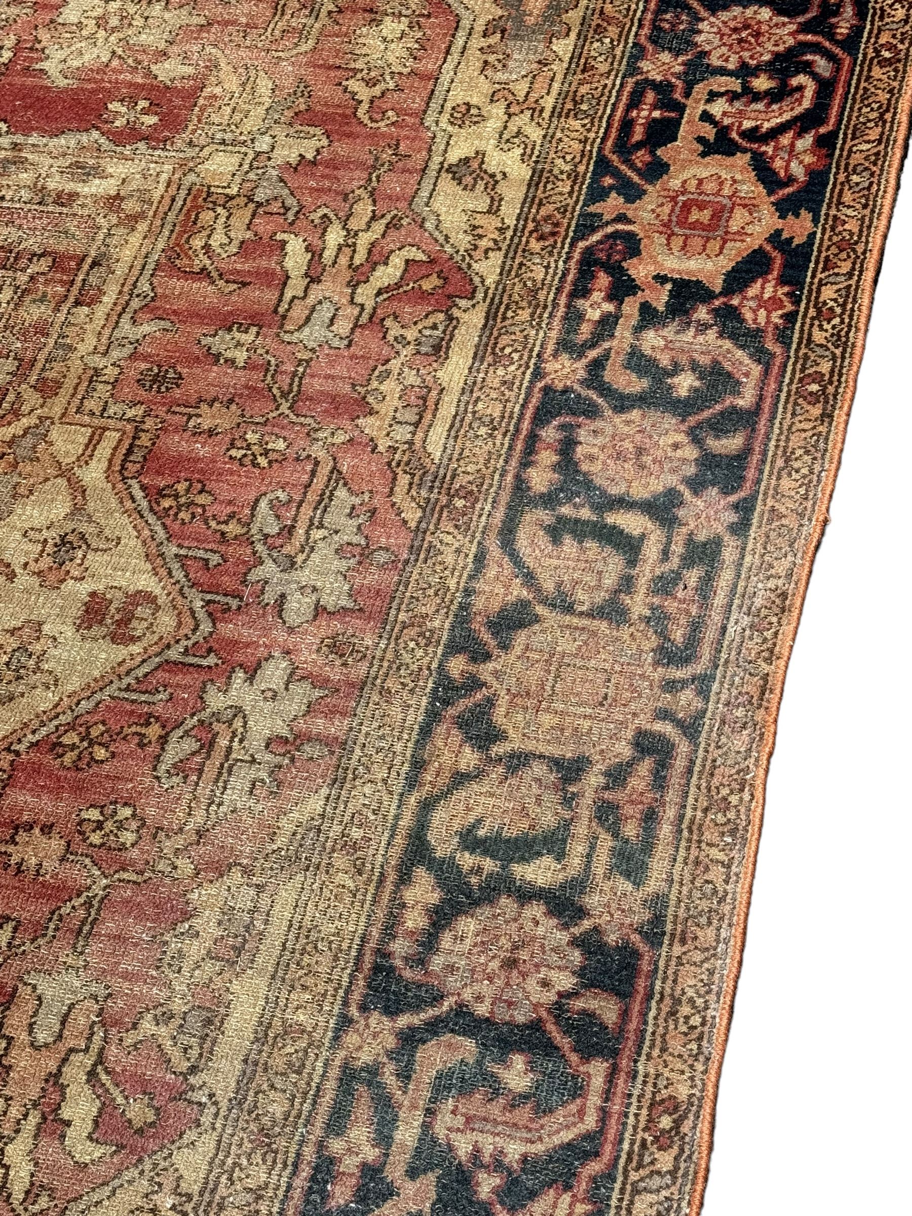 Persian Heriz design rug with red ground, the field featuring a central medallion with floral and geometric motifs, surrounded by ivory spandrels, the main border showcasing a series of floral patterns on a dark blue ground