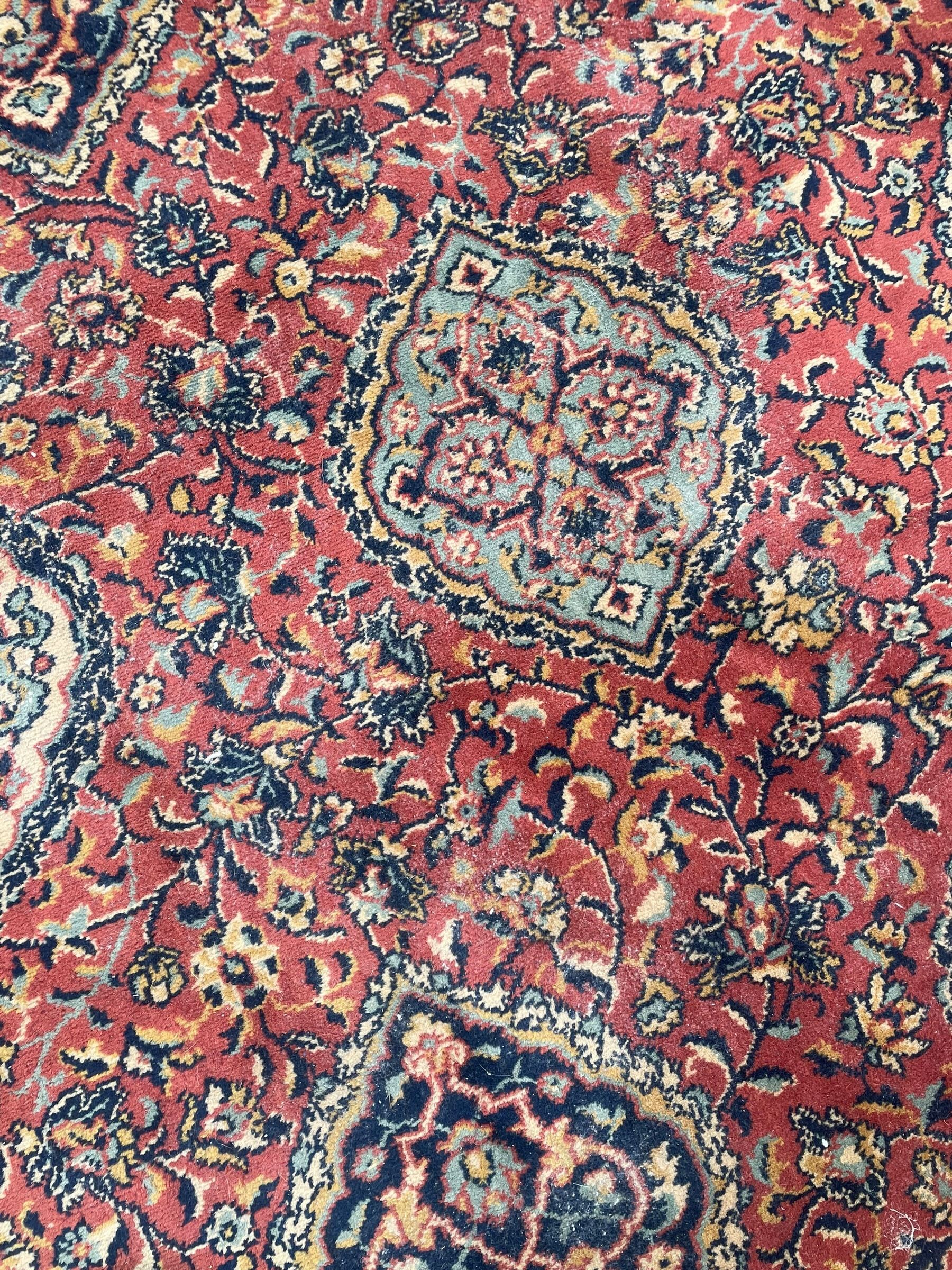 Large Persian design red ground carpet, the field decorated with multiple shaped panels surrounded by trailing leafy branches and stylised plant motifs, the guarded border decorated with shaped panels and floral pattern 