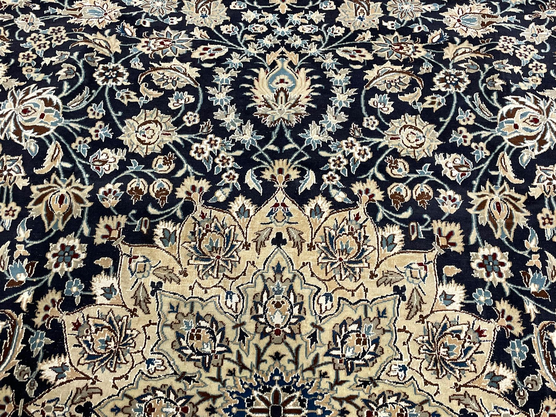 Persian Kashan indigo ground carpet, the central ivory rosette medallion surrounded by trailing and interlaced flower heads and branches, matching spandrels with floral design, the border with scrolling pattern decorated with stylised plant motifs within guards