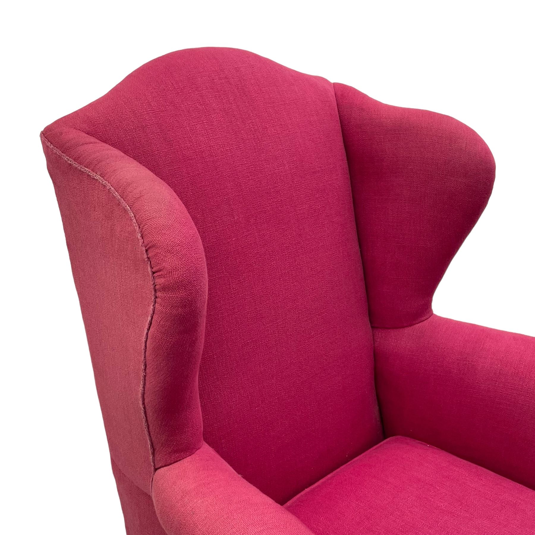 Georgian design hardwood-framed wingback armchair, arched cresting rail over curved wingback, rolled arms on scrolled cushioned supports, reverse bow-front, upholstered in claret red fabric with loose seat cushion, on cabriole front feet and brass castors 