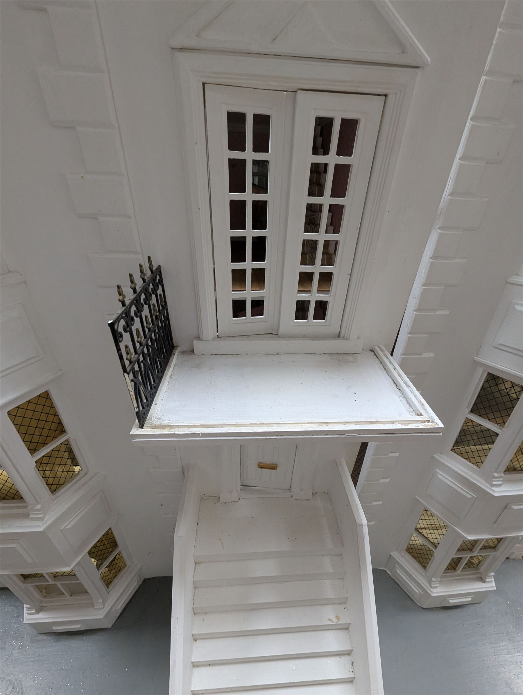 Large three storey modern dolls house, painted white with latticed windows, grey roof and metal fencing, with decorated interior, together with two dolls house garden rooms and two conservatories