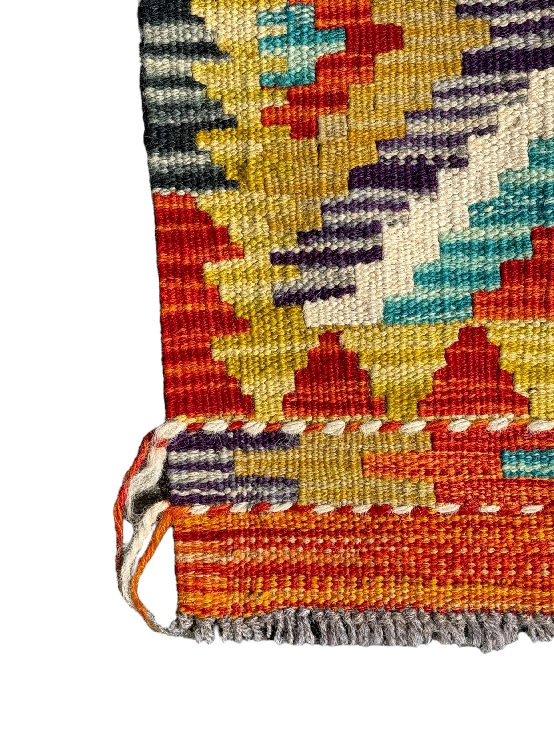 Chobi Kilim ground runner, the field decorated with a geometric pattern of coloured diamonds and triangles, each containing stylised motifs, the shorter ends enclosed by a plain border, and the longer sides with a multicoloured border

