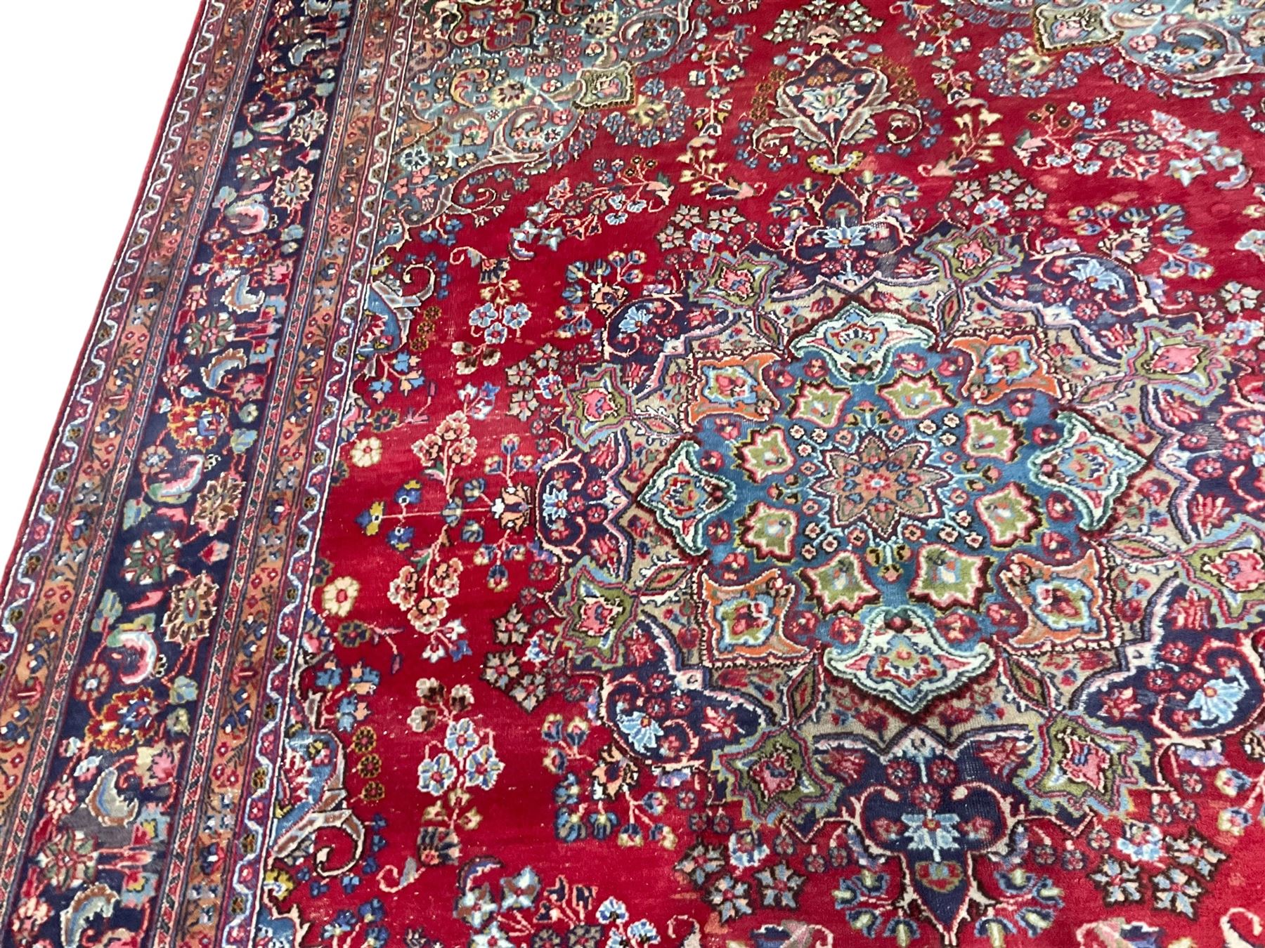 Large Persian Kashan crimson ground carpet, the busy field decorated with a central floral pole medallion surrounded by stylised plant motifs and palmettes with contrasting indigo spandrels, the guarded border decorated with repeating connected foliate designs