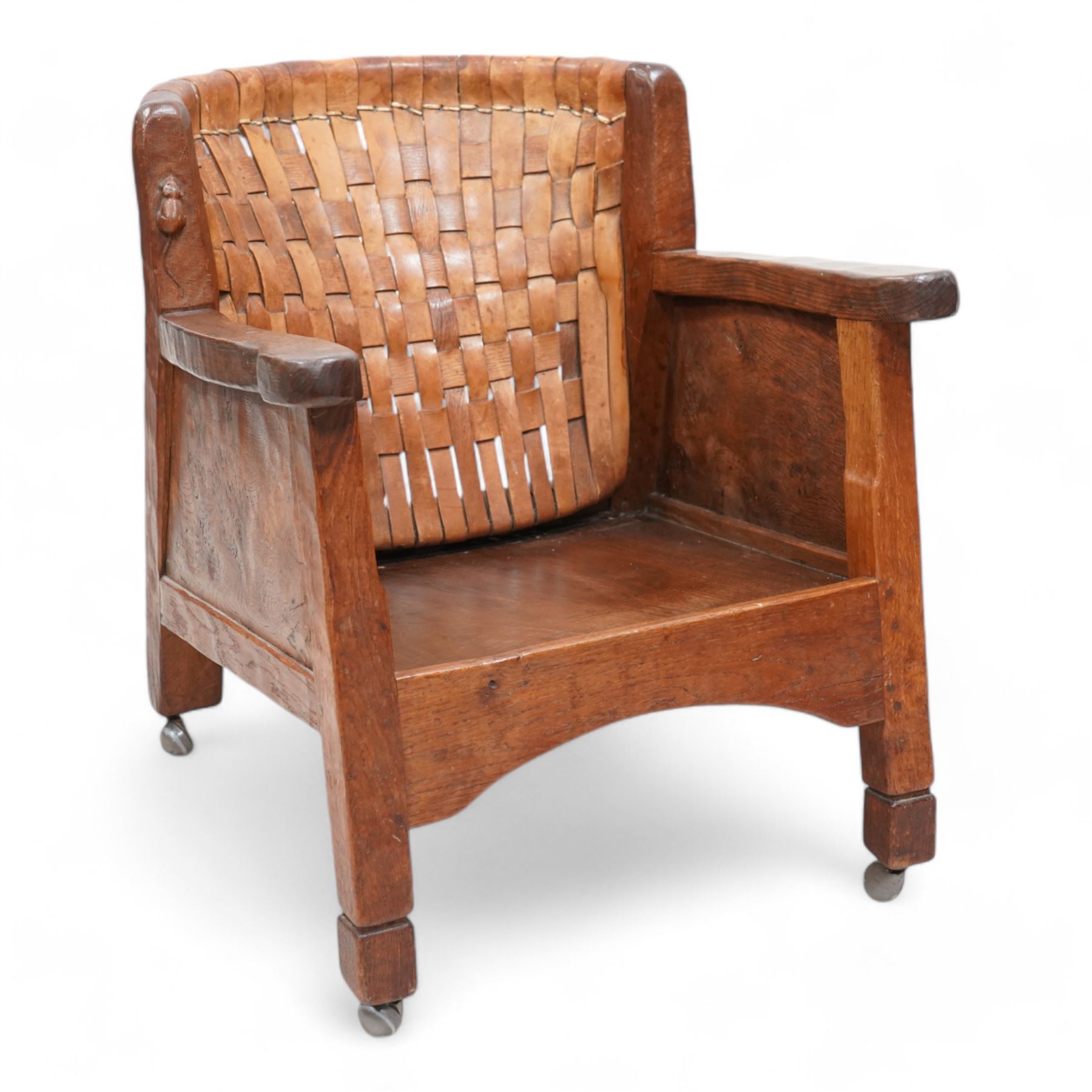 Mouseman - unusual circa. 1930s adzed oak tub-shaped armchair, barrel-back with woven leather, the upright carved with mouse signature, figured panelled sides enclosing panelled seat, arched seat rail, stile supports with block feet on castors, by the workshop of Robert Thompson, Kilburn  

Notes: made by apprentice Graham Hayes (1914-1943). Hayes went on to become a founding member of the Small Scale Raiding Force (SSRF), a special commando unit under the Special Operations Executive (SOE), established by Winston Churchill in 1940. Tragically, he was captured in 1942 and held prisoner by the Gestapo until his execution in 1943. Recently, Hayes has been featured in Guy Ritchie's film 'The Ministry of Ungentlemanly Warfare' under the name 