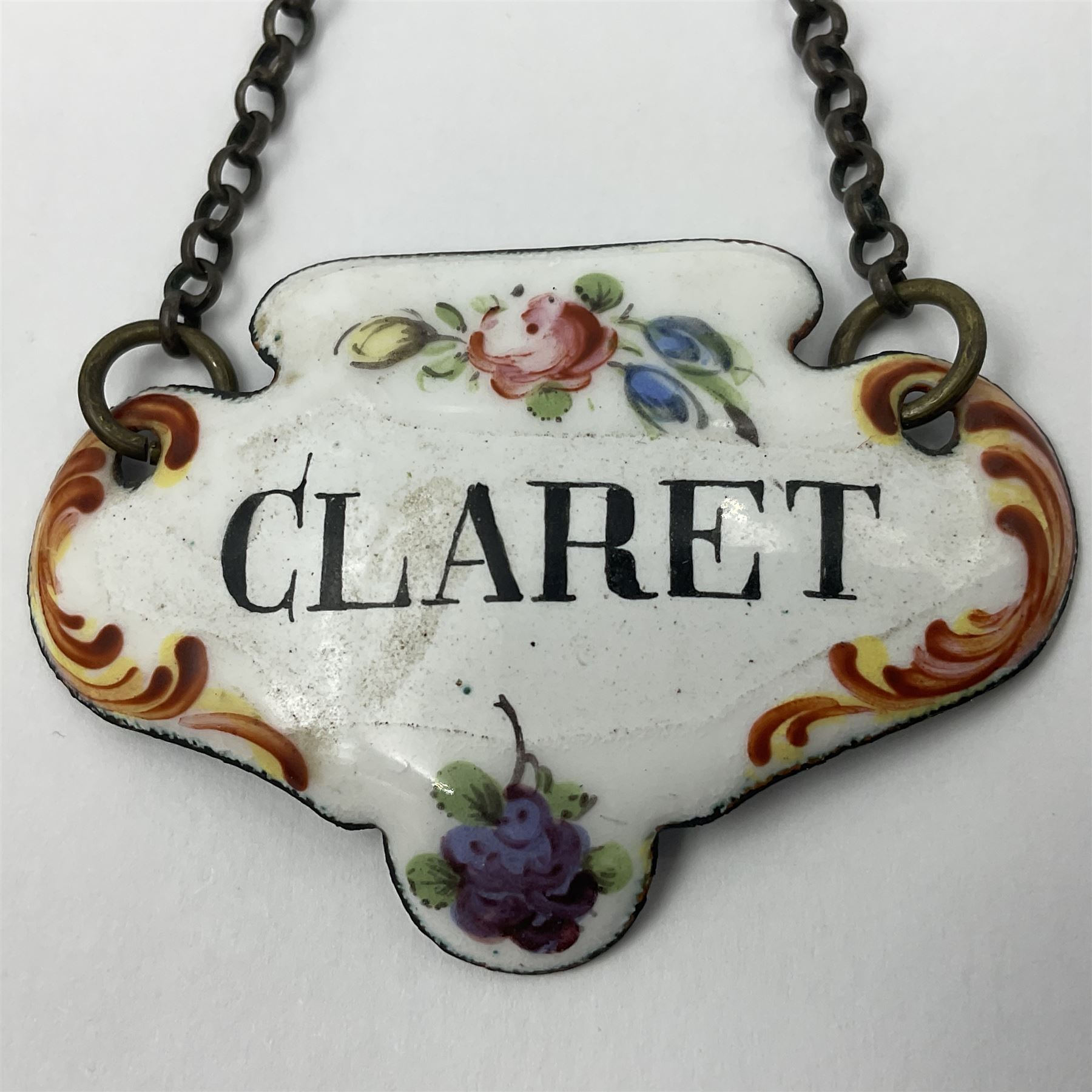 Two late 18th/early 19th century enamel wine labels, each of shaped form, titled 'CLARET', and 'SHERRY' and decorated with floral sprigs and scroll detail upon a white ground, each with suspension chain, each approximately H3.5cm W5cm